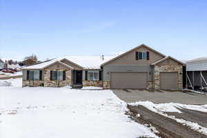 View of front of property featuring a garage, stone siding, and driveway