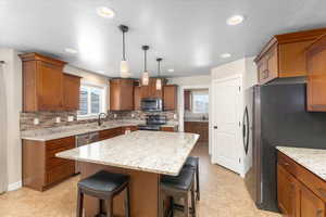 Kitchen featuring a kitchen island, black stainless appliances, decorative backsplash, a kitchen bar, and brown cabinets