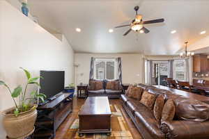 Living room with recessed lighting, lofted ceiling, dark wood-style floors, and ceiling fan with notable chandelier