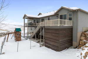 Snow covered rear of property with stairs and a deck