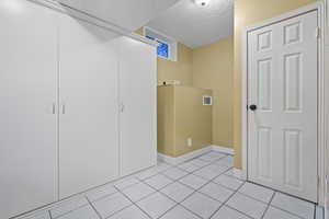 Laundry room featuring light tile patterned floors, visible vents, baseboards, and a textured ceiling