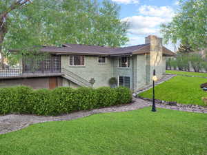 Rear view of house with brick siding, stairway, roof with shingles, a chimney, and a yard