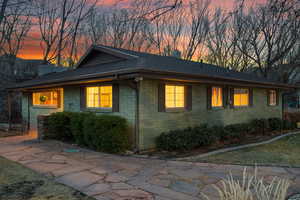 Property exterior at dusk with brick siding, roof with shingles, and a chimney