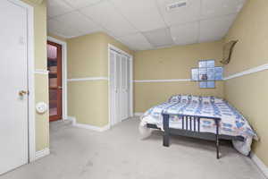 Carpeted bedroom with a wainscoted wall, a closet, visible vents, and a drop ceiling