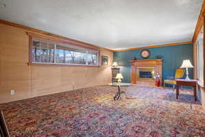 Carpeted living area with visible vents, a fireplace with flush hearth, a textured ceiling, and ornamental molding