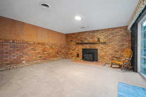 Unfurnished living room featuring visible vents, brick wall, a wood stove, and carpet floors
