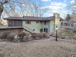Back of property with fence, stairway, roof with shingles, brick siding, and a chimney