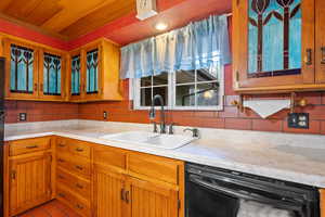 Kitchen with a sink, tasteful backsplash, black dishwasher, wooden ceiling, and light countertops