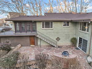 Back of house featuring brick siding, a shingled roof, fence, stairway, and a patio area