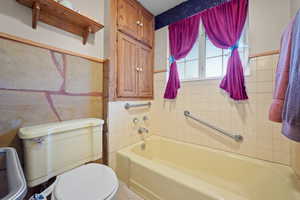 Full bath featuring toilet, tile walls, and a tub to relax in