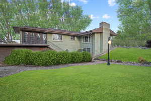 Back of property featuring brick siding, a lawn, and a chimney