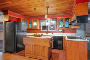 Kitchen featuring a kitchen island, black appliances, light countertops, wood ceiling, and under cabinet range hood