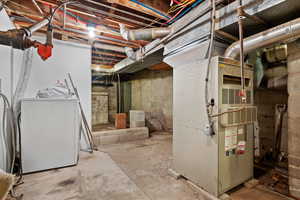 Unfinished below grade area featuring washer / dryer and heating unit