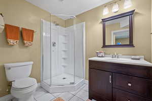 Bathroom with toilet, a stall shower, vanity, and tile patterned flooring