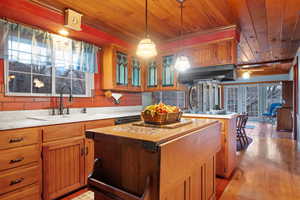 Kitchen featuring a sink, under cabinet range hood, a center island, light countertops, and black electric cooktop