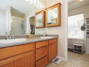 Full bath with a sink, a shower stall, double vanity, baseboards, and a spacious closet