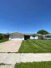 Single story home featuring an attached garage, a front lawn, and concrete driveway