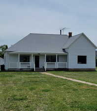 View of front of property with a porch, a front yard, a chimney, and roof with shingles