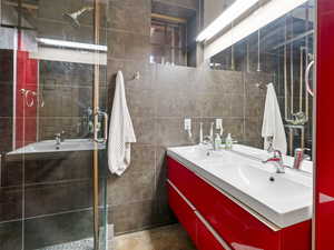 Bathroom with double vanity, tile walls, a stall shower, and a sink