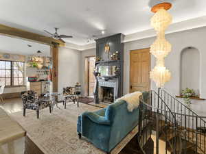 Living area with wood finished floors, baseboards, a fireplace, rail lighting, and ceiling fan with notable chandelier