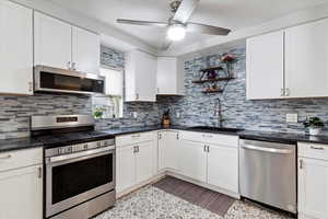 Kitchen featuring ceiling fan, a sink, appliances with stainless steel finishes, white cabinetry, and dark countertops