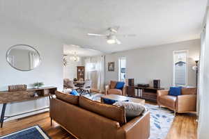 Living room with ceiling fan with notable chandelier, wood finished floors, and a textured ceiling