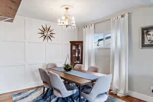 Dining area with a notable chandelier, a decorative wall, baseboards, and wood finished floors