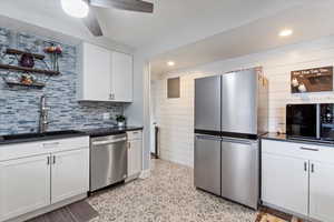 Kitchen with a sink, decorative backsplash, appliances with stainless steel finishes, white cabinetry, and dark countertops