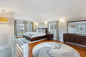 Bedroom with a chandelier, vaulted ceiling, multiple windows, and wood finished floors