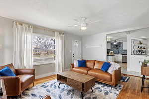 Living area featuring a textured ceiling, light wood-style floors, baseboards, and ceiling fan