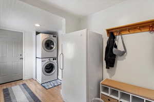 Washroom with laundry area, light wood-style flooring, stacked washer and clothes dryer, and ornamental molding