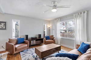 Living room featuring baseboards, a textured ceiling, ceiling fan, and wood finished floors