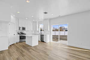 Kitchen with visible vents, light wood-style flooring, appliances with stainless steel finishes, white cabinetry, and a center island