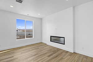 Unfurnished living room featuring visible vents, baseboards, wood finished floors, a glass covered fireplace, and a textured ceiling
