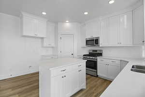 Kitchen with wood finished floors, decorative backsplash, light countertops, appliances with stainless steel finishes, and white cabinetry
