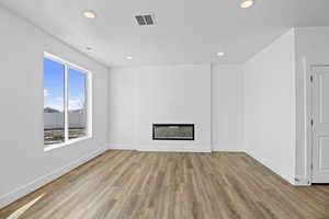 Unfurnished living room featuring light wood-type flooring, visible vents, a glass covered fireplace, recessed lighting, and baseboards