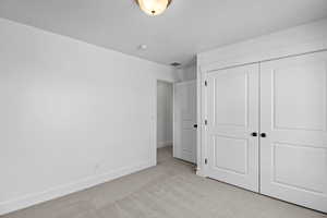Unfurnished bedroom featuring visible vents, light carpet, a textured ceiling, a closet, and baseboards