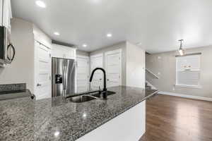Kitchen featuring dark stone countertops, appliances with stainless steel finishes, dark wood-style floors, white cabinets, and a sink