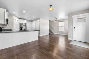 Kitchen featuring dark stone countertops, appliances with stainless steel finishes, a peninsula, and dark wood-style flooring