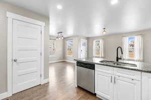 Kitchen with light stone countertops, white cabinetry, a sink, stainless steel dishwasher, and light wood-type flooring