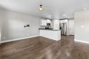 Kitchen featuring baseboards, dark wood finished floors, appliances with stainless steel finishes, a peninsula, and white cabinetry