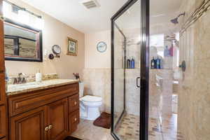 Full bathroom with vanity, a shower stall, toilet, and visible vents