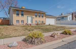 Split foyer home featuring fence, driveway, a chimney, a garage, and brick siding