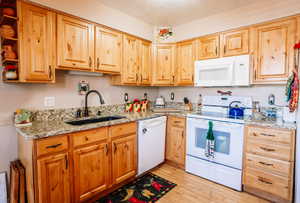 Kitchen featuring a sink, a textured ceiling, white appliances, light wood finished floors, and light stone countertops