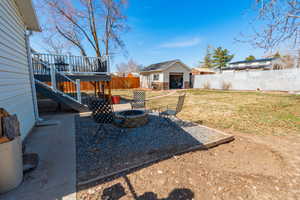 View of yard with a deck, an outdoor structure, a fenced backyard, and a fire pit