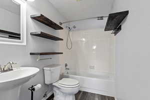 Bathroom with wood finished floors, toilet, a textured ceiling, shower / bathing tub combination, and a sink