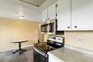 Kitchen featuring light countertops, a textured ceiling, stainless steel appliances, white cabinetry, and baseboards