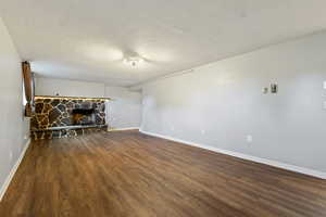 Unfurnished living room featuring a textured ceiling, baseboards, a stone fireplace, and wood finished floors