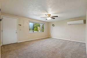 Carpeted empty room featuring baseboards, a ceiling fan, a textured ceiling, and a wall unit AC