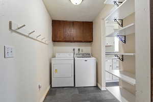 Clothes washing area with a textured ceiling, cabinet space, and washer and dryer